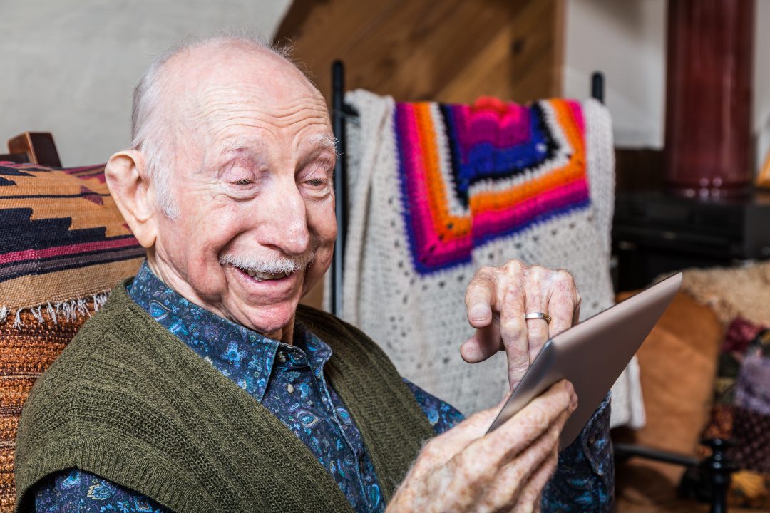 Smiling older gentleman working on a tablet in his living-room